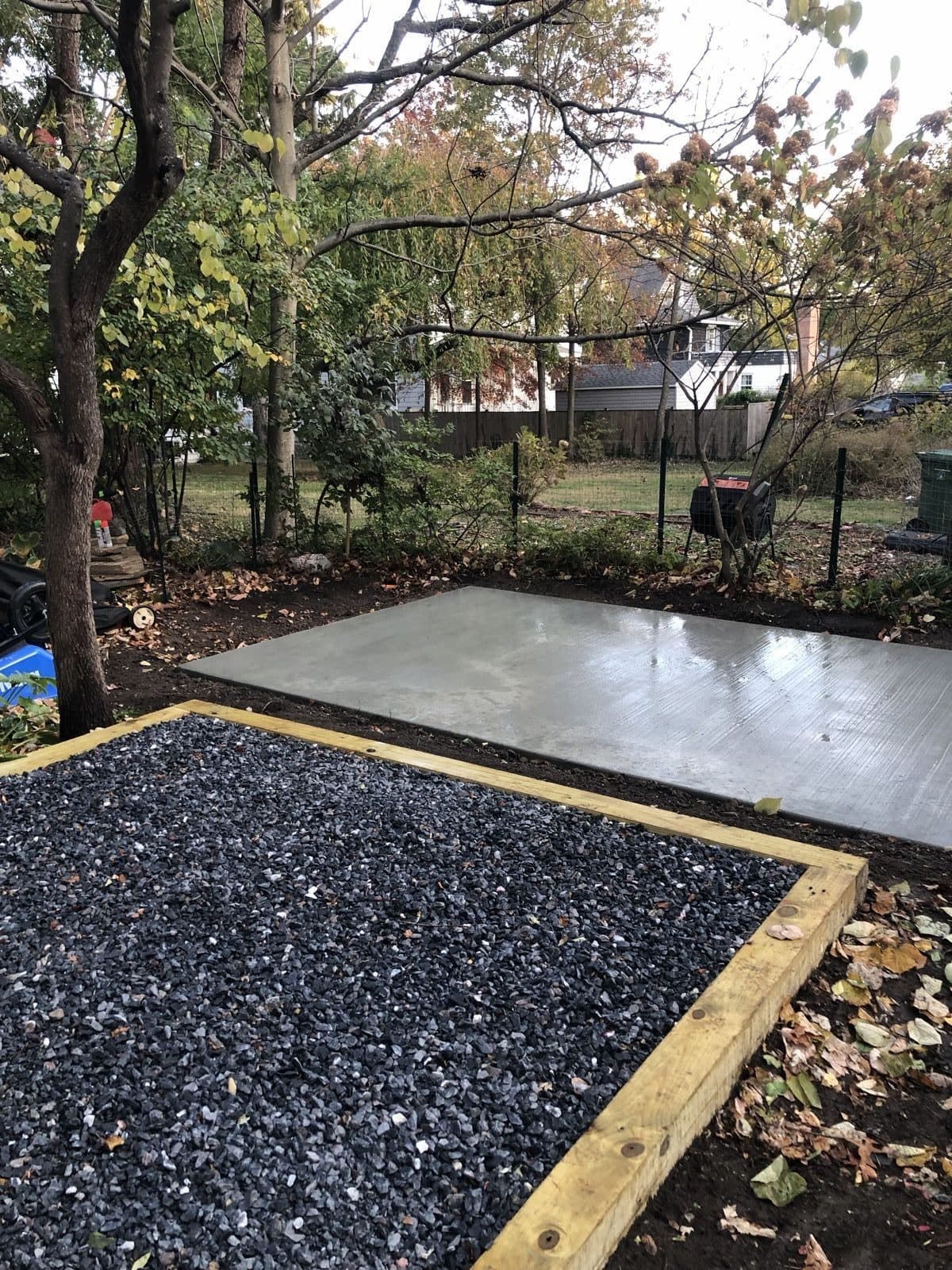 A framed gravel pad and a finished poured-concrete slab built side by side in the same backyard
